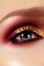 Closeup female eye with fashion bright make-up. Beautiful gold, red eyeshadow, glitter, black eyeliner. Shape Eyebrows