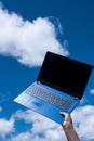 Closeup of female hand holding a blue laptop against the blue sky with white clouds Royalty Free Stock Photo