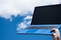 Closeup of female hand holding a blue laptop against the blue sky with white clouds Royalty Free Stock Photo