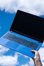 Closeup of female hand holding a blue laptop against the blue sky with white clouds Royalty Free Stock Photo