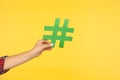 Closeup of female hand holding green paper hashtag symbol, hash sign on yellow background, trending and blogging