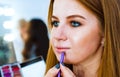 Closeup female hands applying lipstick on cute young red hair woman`s lips using special brush Royalty Free Stock Photo