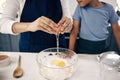 Closeup of female hands cracking a egg into a bowl while baking at home with her son. Woman adding ingredients to a