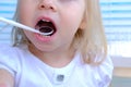 Closeup female hands, dentist, doctor examines oral cavity of small patient, blonde girl 2 years old, molars grow, kid with open