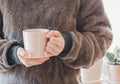 Closeup of female hands with a pink mug coffee beverage. Beautiful girl in grey sweater holding cup of tea or coffee Royalty Free Stock Photo