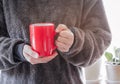 Closeup of female hands with a red mug coffee beverage. Beautiful girl in grey sweater holding cup of tea or coffee in the morning Royalty Free Stock Photo