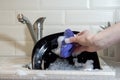 Closeup of female hands washing a black plate with a blue sponge for cleaning against a kitchen sink full of foam Royalty Free Stock Photo