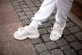 Closeup of female legs in stylish leather white sneakers in trendy white trousers on the street. Modern young woman is standing on Royalty Free Stock Photo