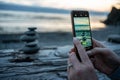 Closeup of a female taking picture of rock cairns on a tree log against the ocean