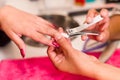 Closeup females hands getting manicure treatment from woman using nailclipper in salon environment, pink towel surface Royalty Free Stock Photo