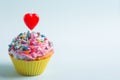 Closeup festive creamy cupcake with sprinkles and candle in form of red heart on light background Royalty Free Stock Photo
