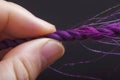 closeup of fingers threading purple wool through needle