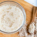Closeup flat top lay view down of soaked rice, grain, cloudy liquid water in glass bowl on wooden background Royalty Free Stock Photo