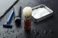 Closeup of foam, tube, brush, razor for shaving on the wet dark surface