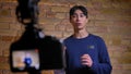 Closeup focused shoot of camera recording young korean male videoblogger talking and gesturing refocusing on the speaker