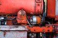 Closeup of four cylinder diesel tractor engine with visible belt rusty tracks hydraulic parts and wiring red paint in