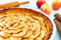 Closeup on a French apple tart aside Gala apples, cinnamon sticks and a rolling pin on a light blue background. Side view Royalty Free Stock Photo