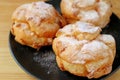 Closeup French Cream Puffs on Black Plate Sprinkled with Icing Sugar