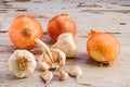 Closeup of fresh bulbs of onion and garlic resting atop a rustic wooden table