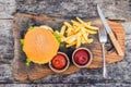 Closeup of fresh burger with French fries on wooden table with bowls of tomato sauce. lifestyle food Royalty Free Stock Photo