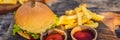 Closeup of fresh burger with French fries on wooden table with bowls of tomato sauce. lifestyle food BANNER, LONG FORMAT Royalty Free Stock Photo