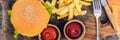 Closeup of fresh burger with French fries on wooden table with bowls of tomato sauce. lifestyle food BANNER, LONG FORMAT Royalty Free Stock Photo