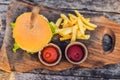 Closeup of fresh burger with French fries on wooden table with bowls of tomato sauce. lifestyle food Royalty Free Stock Photo