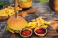 Closeup of fresh burger with French fries on wooden table with bowls of tomato sauce. lifestyle food Royalty Free Stock Photo