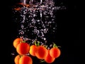Closeup of fresh and health cherry tomatoes falling into clear water with big splash on black background. Group of fresh tomatoes Royalty Free Stock Photo