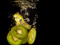 Closeup of fresh kiwis slices falling into clear water with big splash on black background. Group of juicy kiwi falling into water