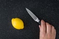 Closeup of fresh lemon on a black cutting board, paring knife, womanÃ¢â¬â¢s hand