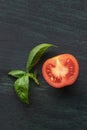 A closeup of a fresh organic heirloom tomato with vibrant green basil leaves, shot from the top on a dark background Royalty Free Stock Photo