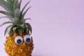 Closeup of fresh pineapple with green leaves and googly eyes on pink background,