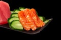 Closeup of raw salmon sashimi on platter with tuna and cucumber on black background Royalty Free Stock Photo