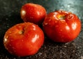 Closeup of fresh ripe tomatoes with water droplets on a black granite kitchen counter surface Royalty Free Stock Photo
