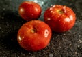 Closeup of fresh ripe tomatoes with water droplets on a black granite kitchen counter surface Royalty Free Stock Photo