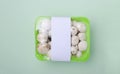 Closeup and top view of packaged white mushrooms in the box on the bright green surface.Blank tag for price Royalty Free Stock Photo