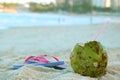 Closeup a fresh young coconut on the sandy beach with blurry pink sandals in background Royalty Free Stock Photo