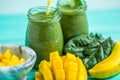 Closeup freshly blended green smoothie with mango and banana in glass jars. Turquoise blue table