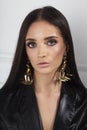 Closeup front of a brunette woman with makeup, wear masive earrings, looking at camera, isolated white background.