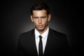 Closeup front portrait of a handsome confident businessman wearing suit standing isolated over black background.