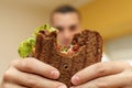 Closeup funny blurred protrait of young man hold bitten sandwich by his two hands. Sandwich in focus. light background