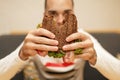 Close up funny blurred protrait of young man hold bitten sandwich by his two hands. Sandwich in focus. light background