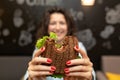 Closeup funny blurred protrait of young woman hold bitten sandwich by her two hands. Sandwich in focus. dark background