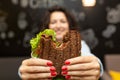 Closeup funny blurred protrait of young woman hold bitten sandwich by her two hands. Sandwich in focus. dark background Royalty Free Stock Photo