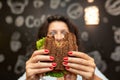 Closeup funny blurred protrait of young woman hold bitten sandwich by her two hands. Sandwich in focus. dark background