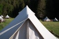 Closeup of glamping tent top white fabric in green meadow surrounded by fir tree forest Royalty Free Stock Photo