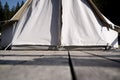 Closeup of glamping tent white fabric entrance on wooden deck in green meadow surrounded by fir tree forest Royalty Free Stock Photo