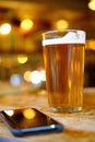Closeup of a glass of beer on the table near a phone under the lights with a blurred background Royalty Free Stock Photo