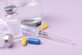 Closeup of glass bottles of liquid medicine, capsules, syringe and glass of water on the pink desk Royalty Free Stock Photo